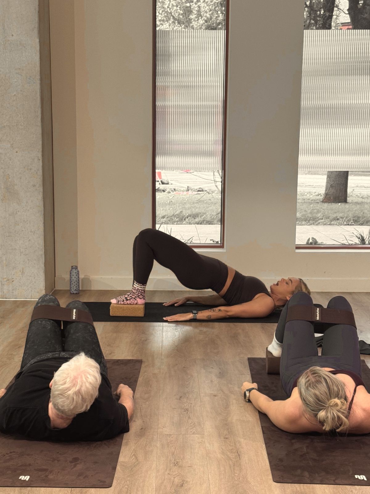 Aoife demonstrating a single-leg bridge on a cork block while two participants with bands watch