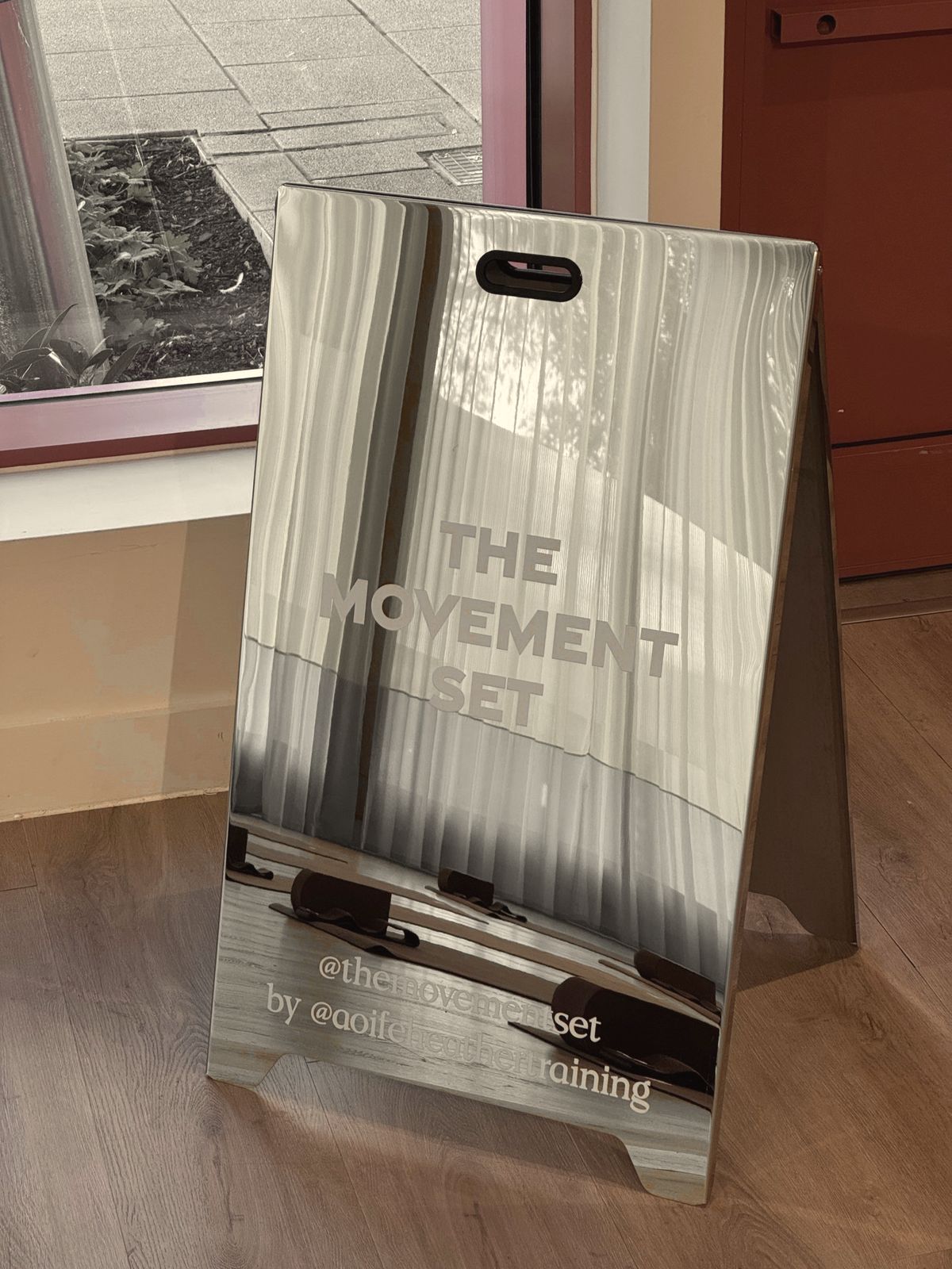 The Movement Set mirror sign reflecting lime curtains and mats laid out for class