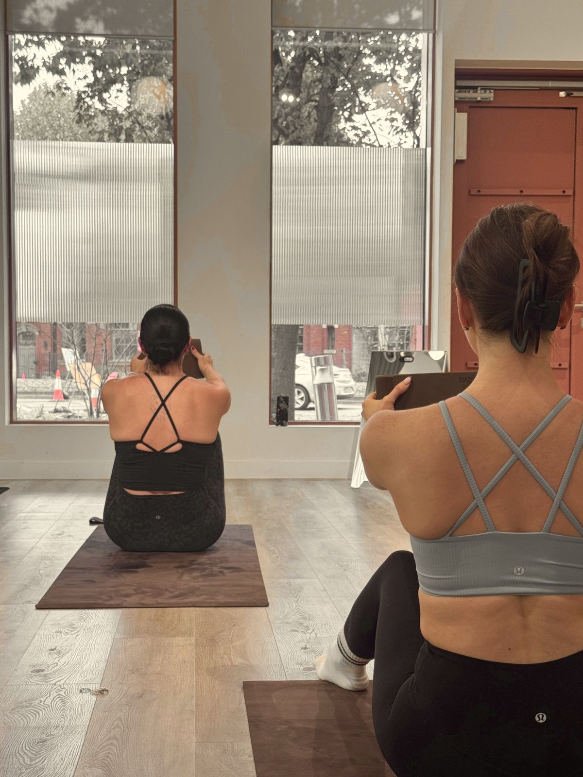 Two participants seated on brown mats holding blocks out in front, facing tall ribbed-glass windows